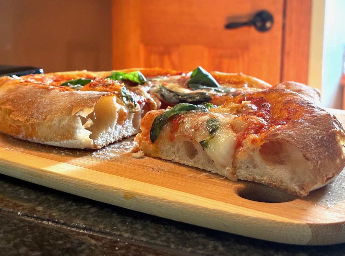 Basil and mozzarella pizza slices with an airy golden crust on a wooden board