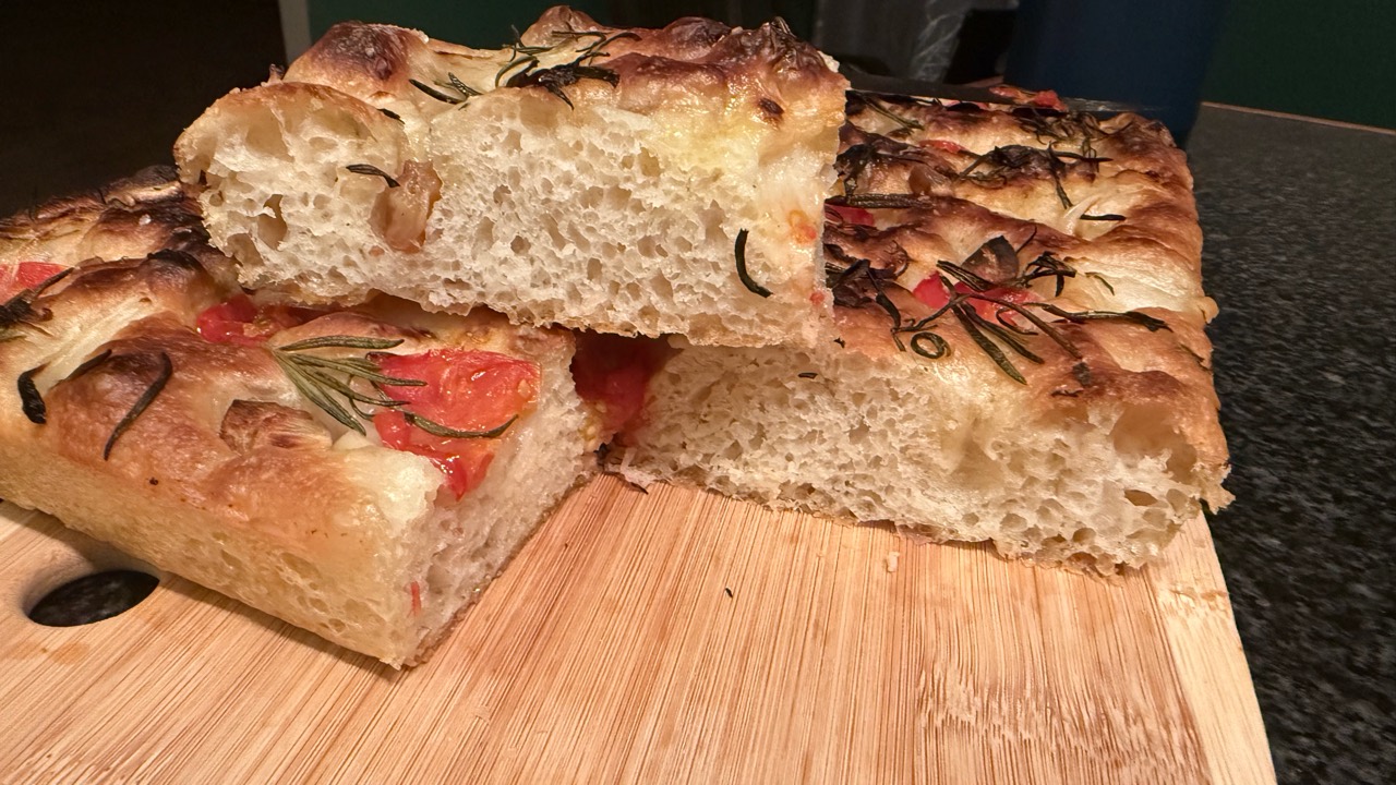 Slices of golden focaccia with tomatoes, rosemary, and an airy crumb